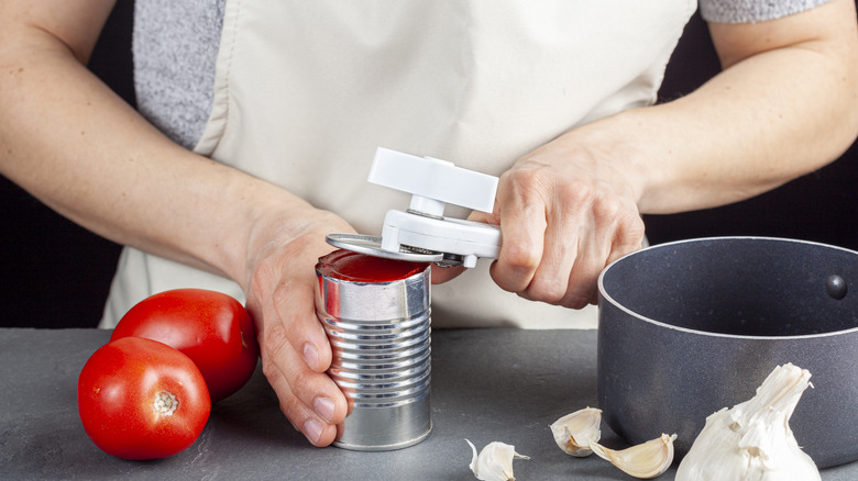 Person using a manual can opener to open tomato sauce