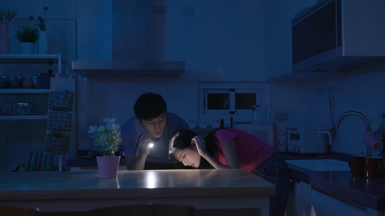 Asian couple uses flashlight to search through drawers while lights are off