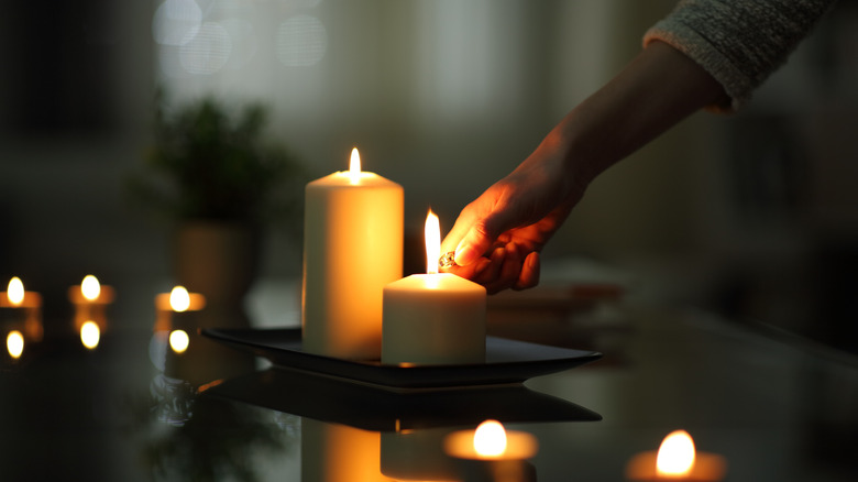 Person lighting a candle in a dark room, one candle already lit