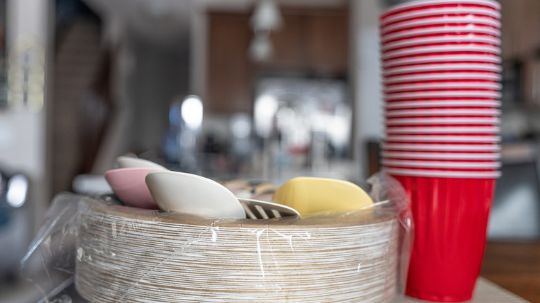 Stack of paper plates with utensil and red plastic cups next to them
