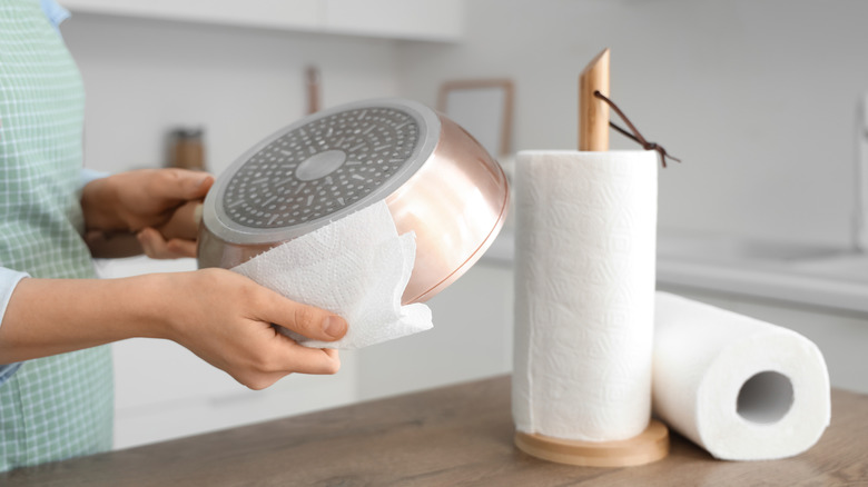 Person in a green and white checkered shirt wiping pot with paper towels