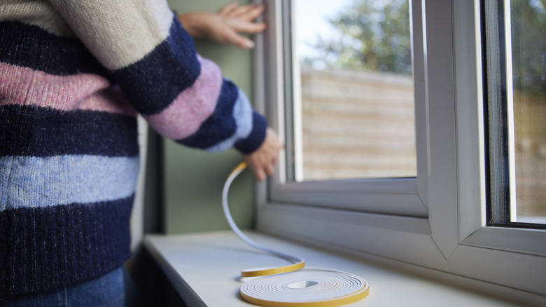 Person in striped sweater applying window insulation material to window