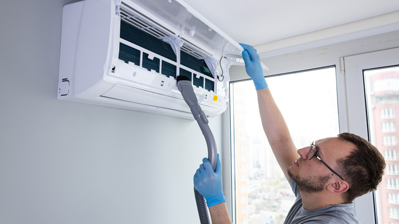 A person cleaning the interior parts of an air conditioner with a vacuum cleaner and brush attachment