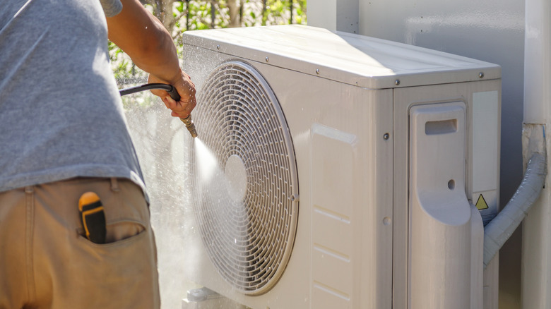 A person cleaning an outdoor air conditioner unit with a hose