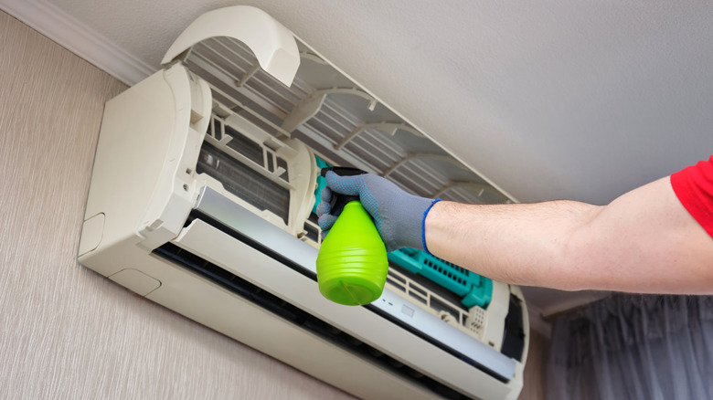A person spraying an air conditioner unit to clean mold