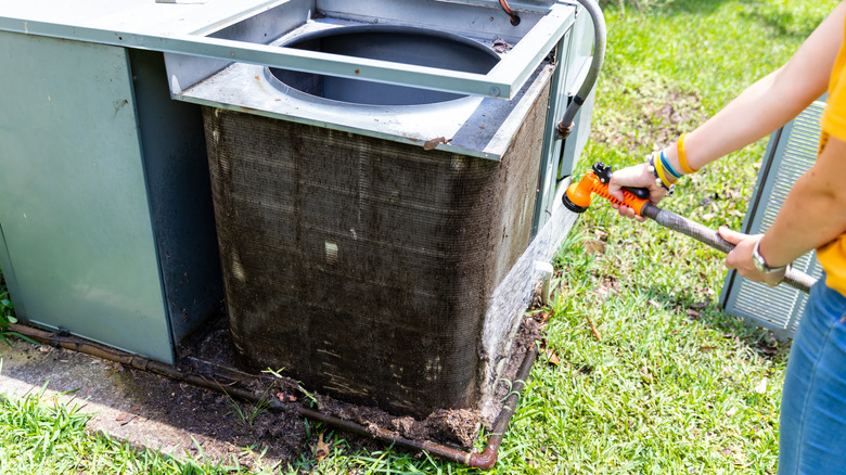 A person using a hose to gently clean their outdoor AC unit