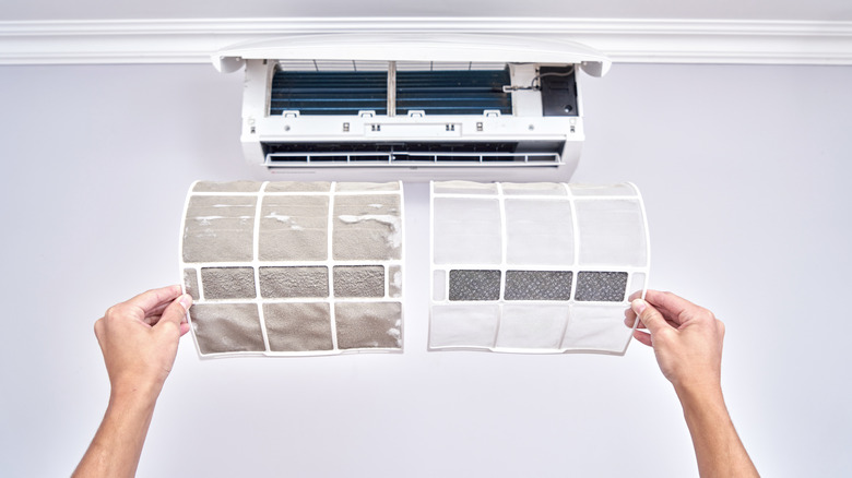 A person holding up two air conditioning filters, one dirty, and one clean
