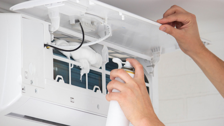 A person cleaning an air conditioning unit with specialized cleaning foam