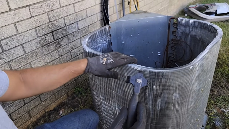 A person using a fin comb to straighten bent fins on a home HVAC system
