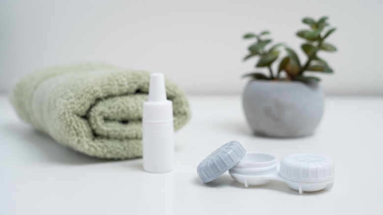 Contact lens case and bottle on a counter next to a towel and plant