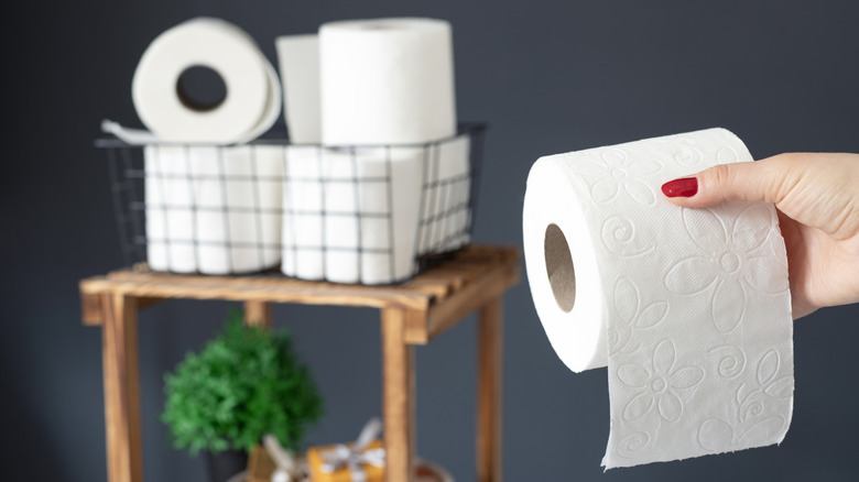 Person grabbing a roll of toilet paper from bathroom basket