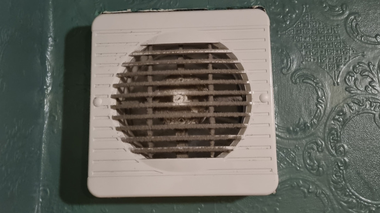A small, dirty exhaust fan in an old bathroom.