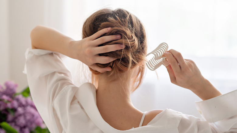 A woman puts a white plastic hair clip on her hair.