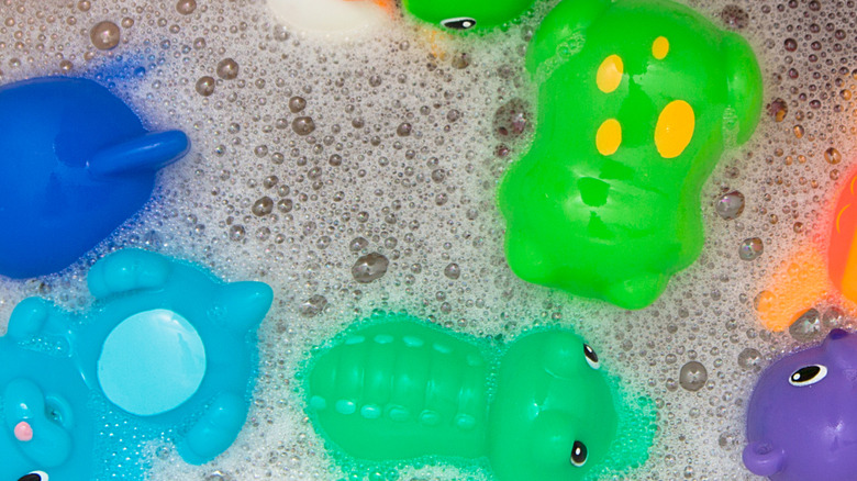 Several colorful bath toys in a tub filled with soap bubbles.