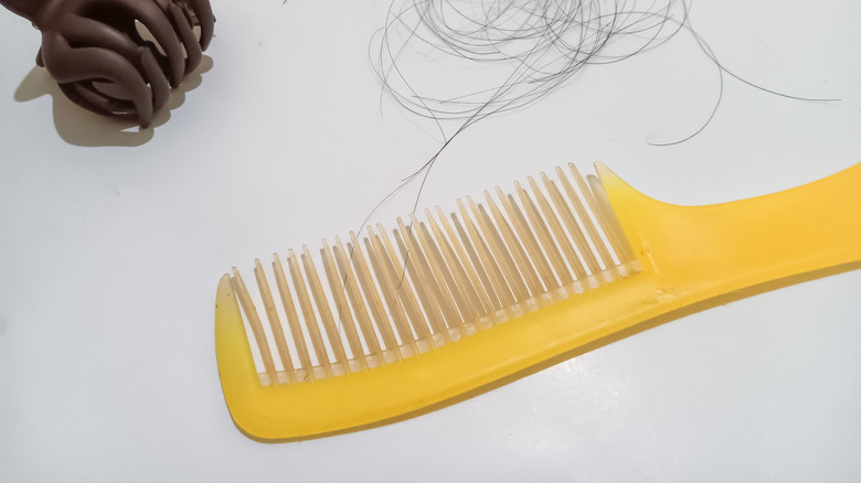 A plastic yellow hairbrush near hair and a clip.