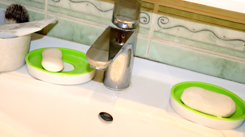 Two white and green plastic soap dishes on either side of a bathroom sink faucet.