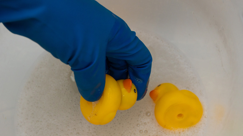 A blue gloved hand with two rubber duck toys in soapy water
