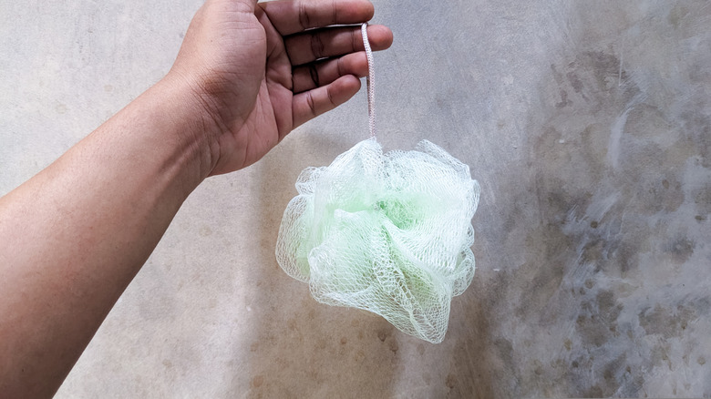 A hand holding a light green shower loofah