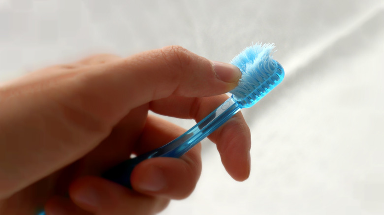 A hand holding a blue toothbrush with frayed bristles