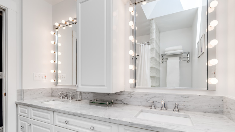 White bathroom with bulb framed mirrors and silver finishings
