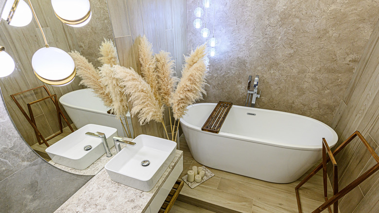 A modern bathroom with a large vase of pampas grass next to a soaking tub