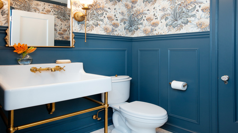 A bathroom with blue wainscoting and wallpaper.