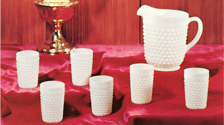 Hobnail milk glass pitcher and cups on a red cloth