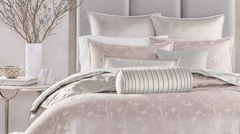 a bed with lots of fluffy pillows and a pink duvet cover sitting atop a bed with an end table next to it