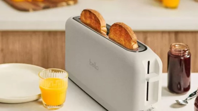Bella two slice toaster from Macy's sitting on a countertop with jelly and a glass of orange juice nearby. two pieces of toast are popping up out of the toaster