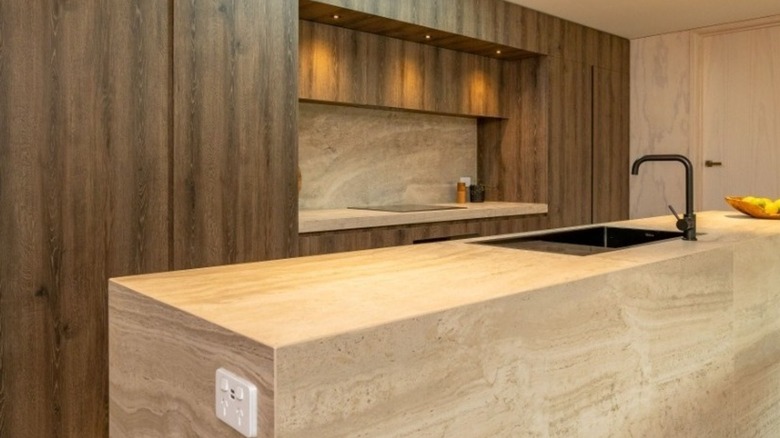 A modern kitchen with Travertine and dark wooden cabinets and a Travertine island