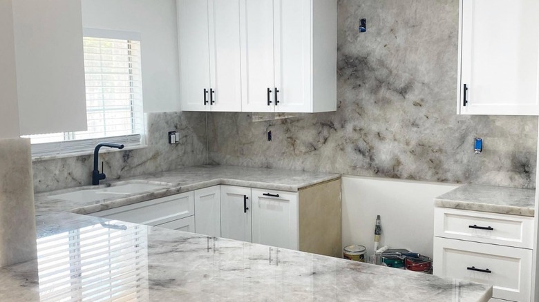 A white quartzite slab backsplash in a newly renovated kitchen with white cabinets