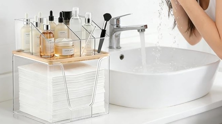 A facial towel holder beneath an acrylic makeup organizer on a bathroom counter
