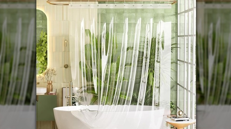 A clear curtain liner draped over the side of a white bathtub