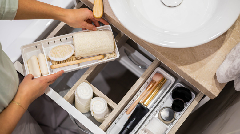 Woman using organizers to declutter vanity drawer in bathroom