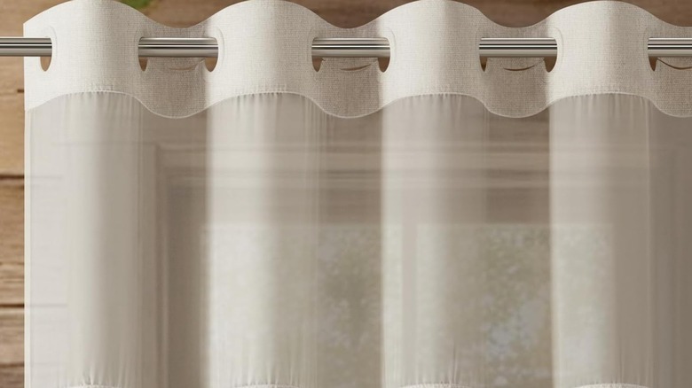 A beige shower curtain with mesh detailing on top