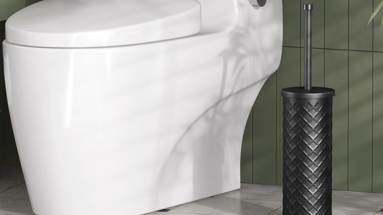 A black toilet brush inside a black holder near a white toilet