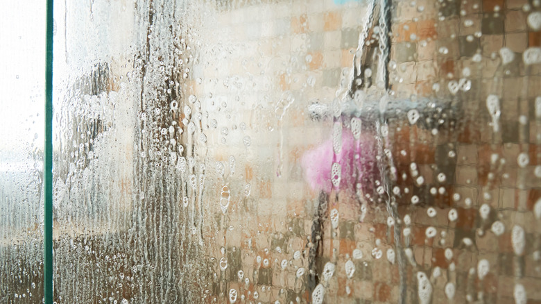 closeup on soapy clear glass shower door with notable green hue on edges