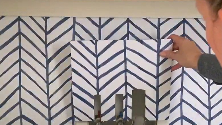 Woman placing wallpaper square over washing machine hookups
