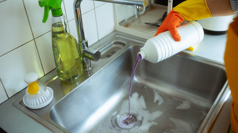 person wearing gloves while pouring chemical into sink