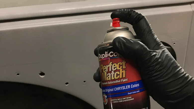 A gloved hand using a can of Dupli-Color Perfect Match paint to touch up a car