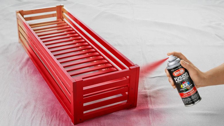 Hand using Krylon spray paint to paint a wood tray red