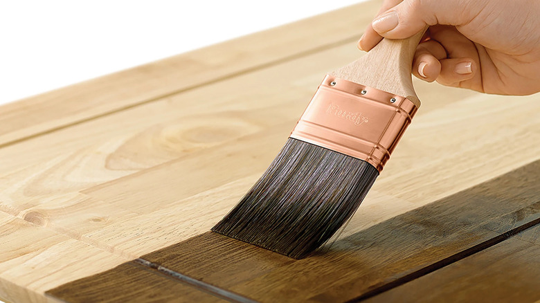 Hand applying a Minwax stain to a piece of wood with a Purdy brush