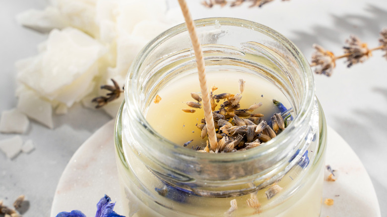 A candle has a long wick and lavender sprinkled on top.