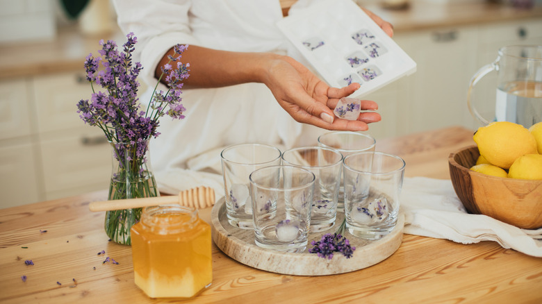 A woman adds lavender ice cubes to a group of glasses.