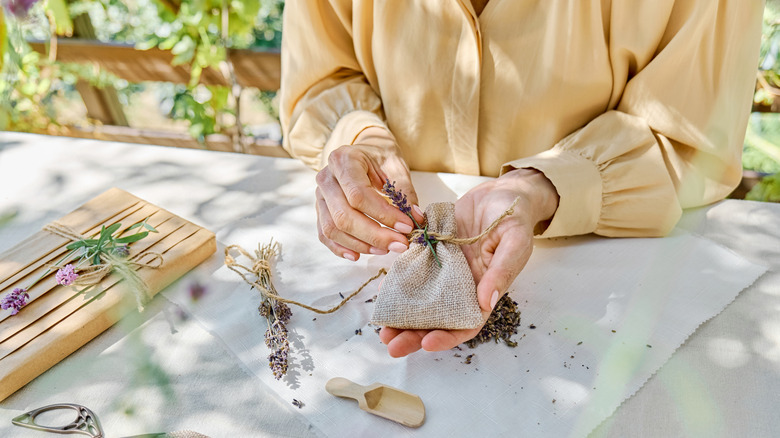 A person in a yellow shirt holds a small burlap sachet with a sprig of lavender.