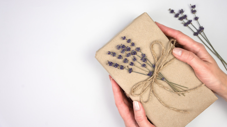 A gift is wrapped in brown paper with a twine bow holding sprigs of lavender.