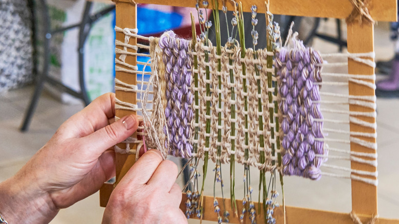 A person weaves a small square using thread and lavender stalks.