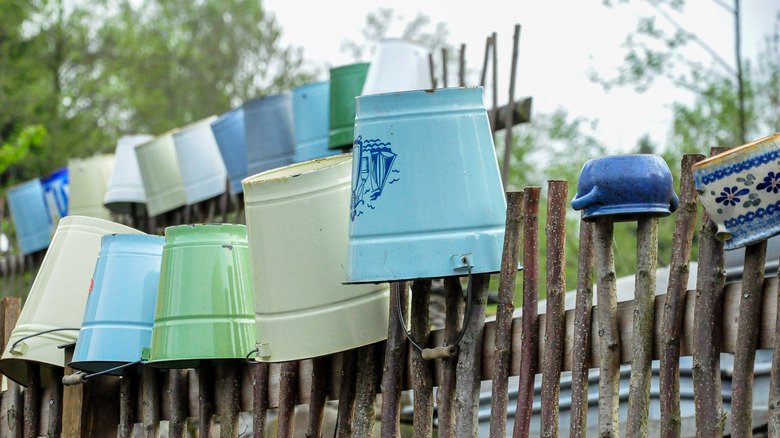 A group of inverted buckets and planters line a garden fence