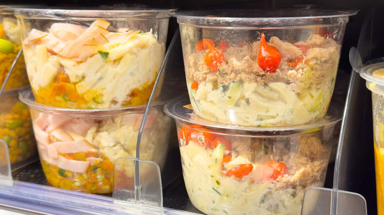 Deli containers at the supermarket are filled with cold salads and stacked on shelves