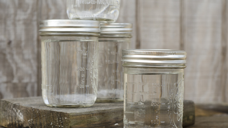 A group of mason jars are seen outside lined up on an old board